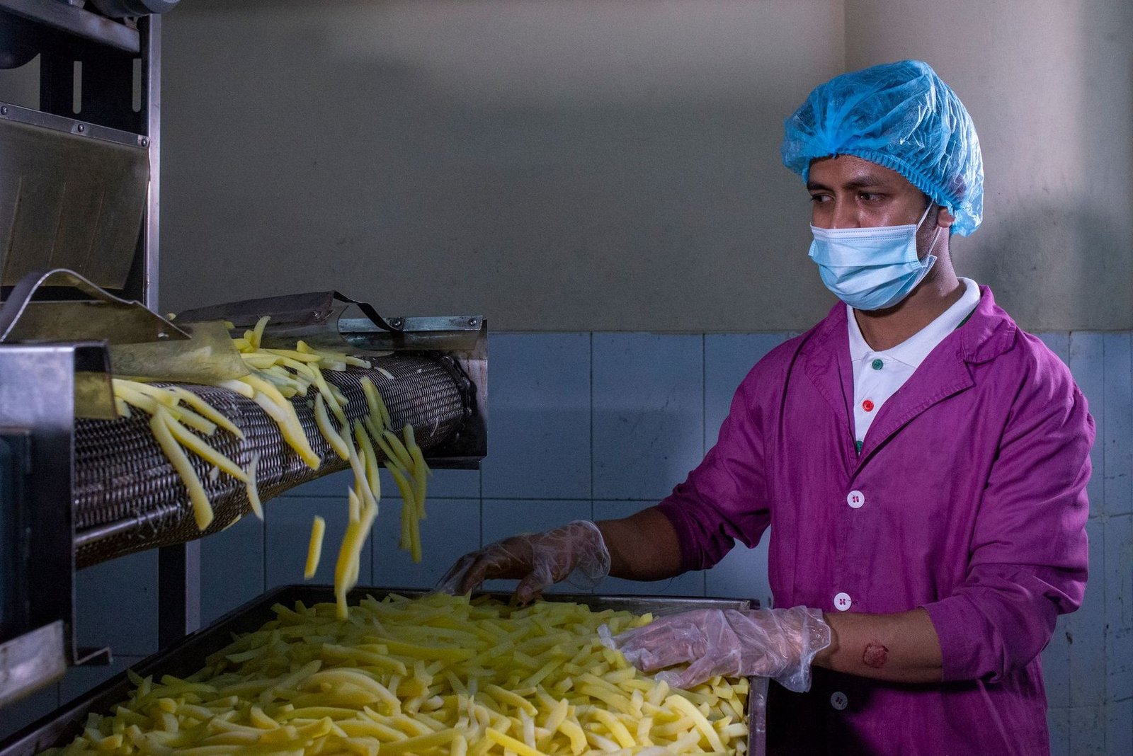 Food-production worker in hairnet, mask and gloves checking fresh product on a processing line